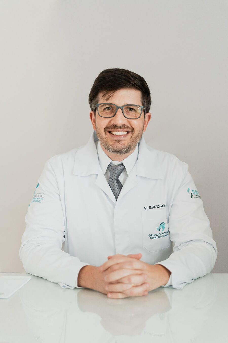 Dr. Carlos Eduardo Bastiani sentado à mesa do consultório, sorrindo